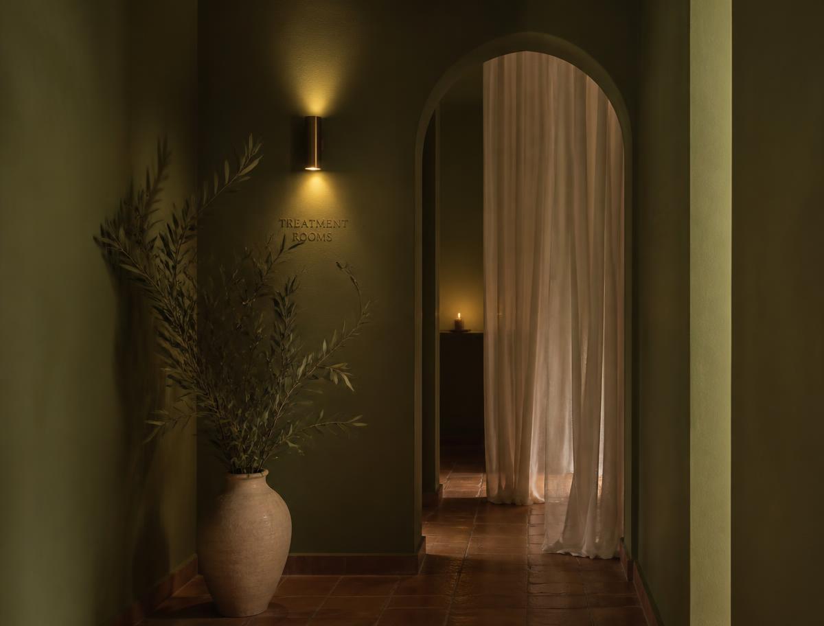 Corredor do spa com paredes verde-oliva, arco e cortina de linho iluminada